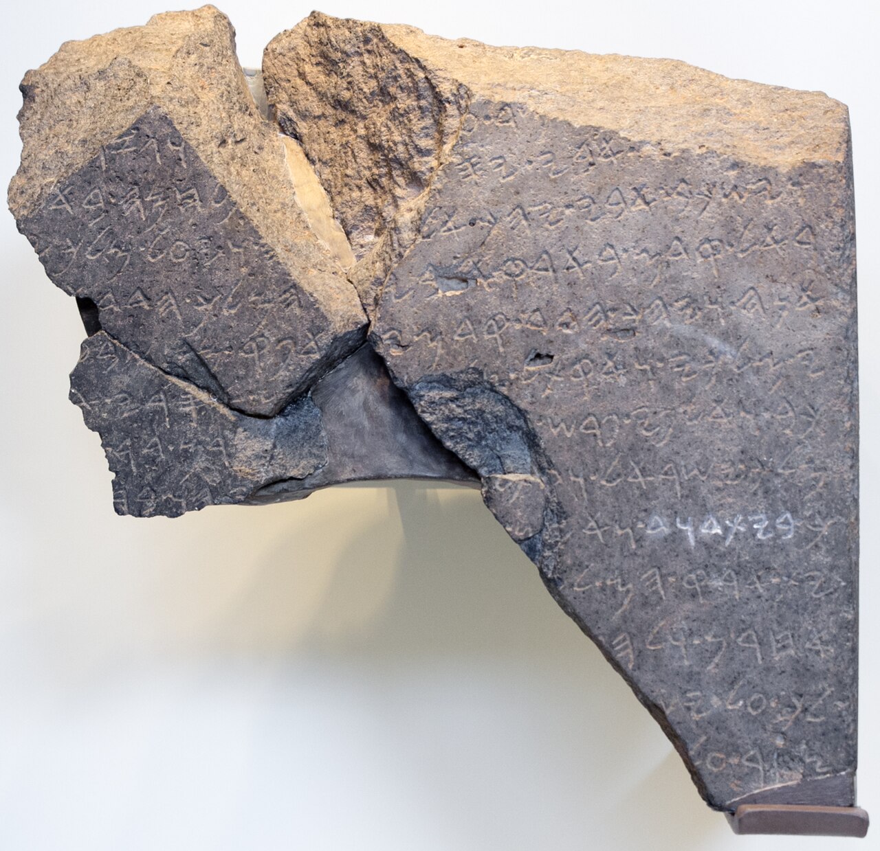 The Tel Dan Stele in the Israel Museum — three joined fragments of dark basalt bearing incised lines of Old Aramaic letters, the breaks between the fragments clearly visible.