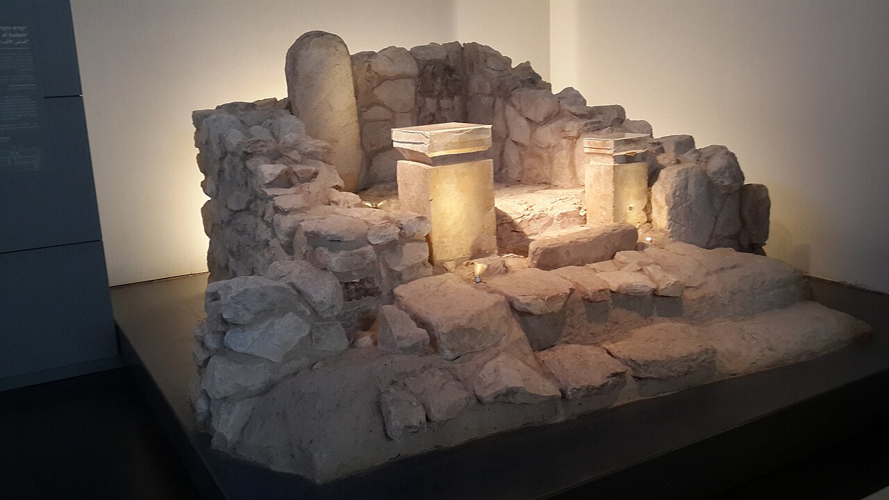 The Holy of Holies from the Arad sanctuary as reconstructed in the Israel Museum — a small niche approached by steps, flanked by two stone incense altars, with a smooth rounded standing stone at its back.
