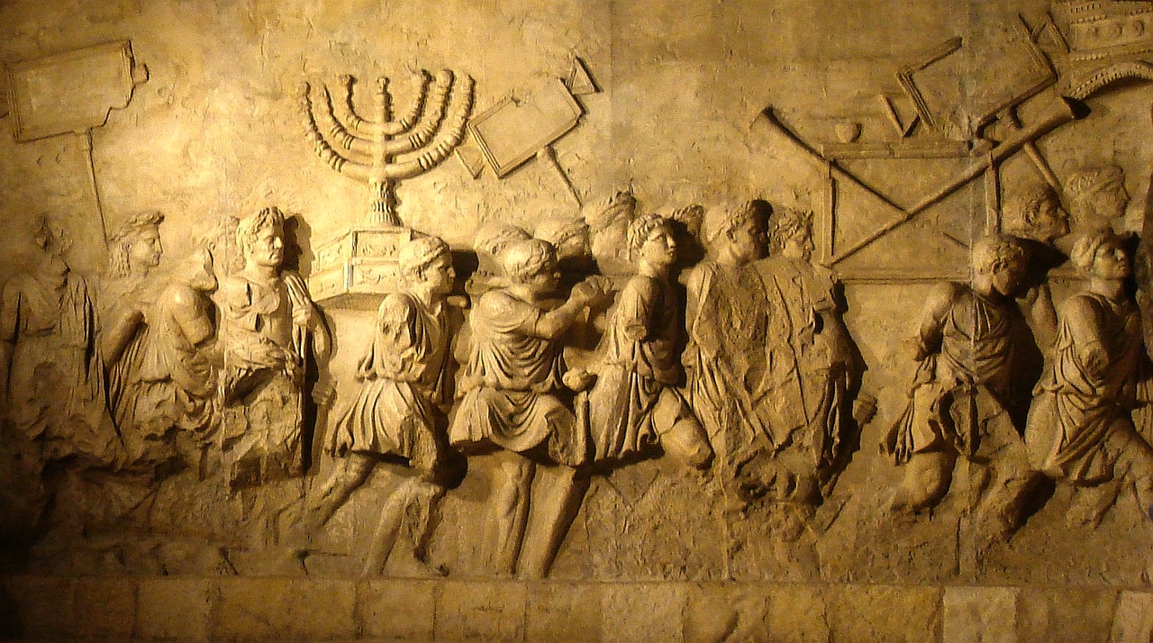 The spoils relief on the Arch of Titus in Rome — Roman figures in procession carrying the seven-branched menorah of the Temple on a litter, with the shulchan and trumpets beside it.
