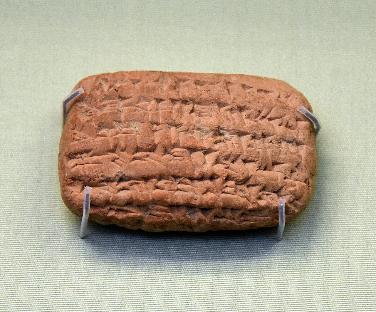 The Nebo-Sarsekim tablet in the British Museum — a small rounded-cornered clay tablet covered in compact lines of cuneiform, held on display mounts.
