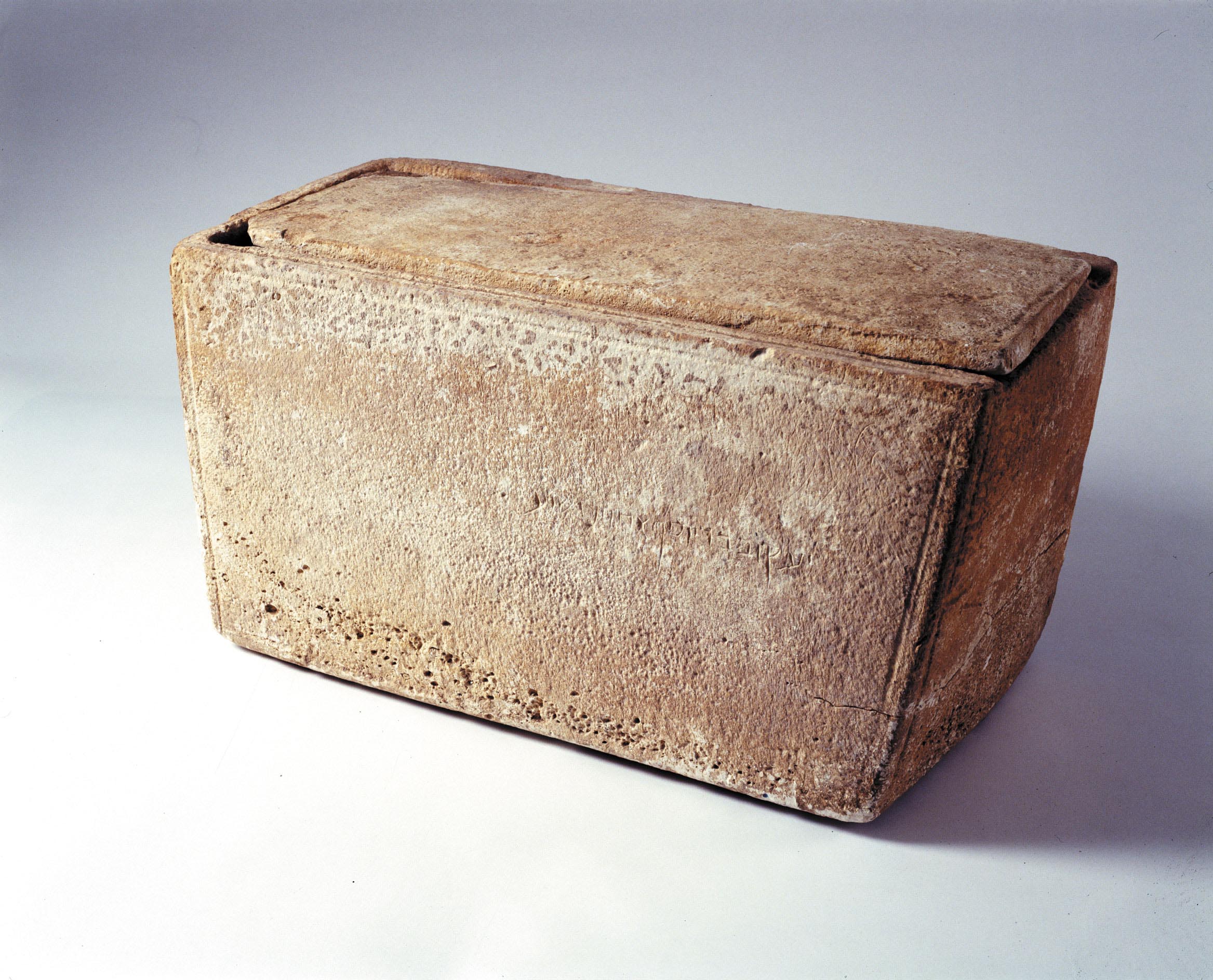 The James Ossuary on display — a pale rectangular limestone bone box with a shallow incised Aramaic inscription running along one long side.
