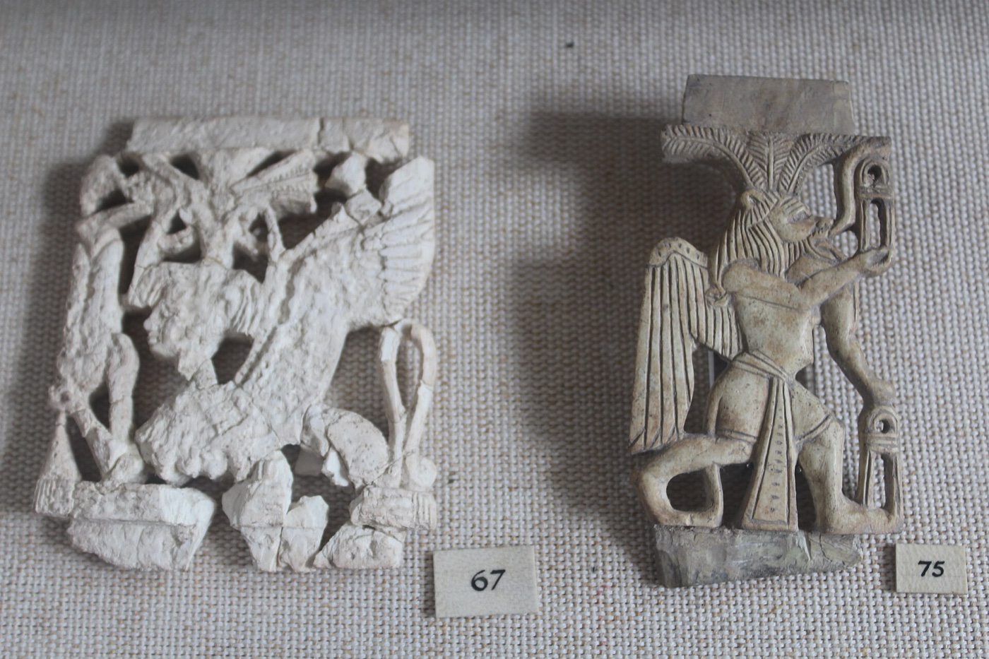 Two carved ivory plaques from the Megiddo hoard in a museum display case — an openwork plaque with winged sphinx figures and a plaque of a winged griffin-like figure amid palmettes.
