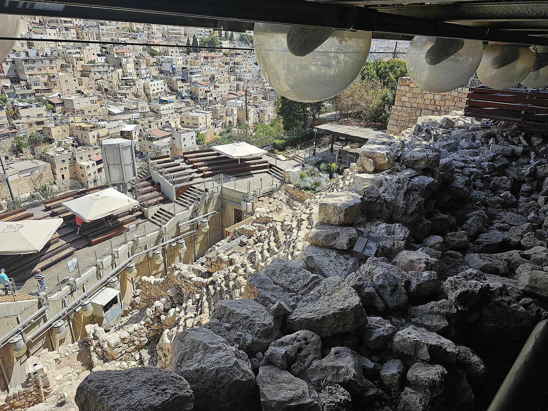 The wall of the Large Stone Structure in the foreground, overlooking the terraced stone mantle of the Stepped Stone Structure descending the City of David's eastern slope.
