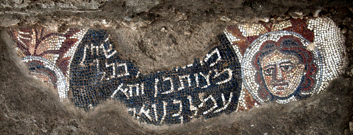 Detail of the Huqoq synagogue mosaic — a woman's face beside a Hebrew inscription medallion, in richly colored tesserae.
