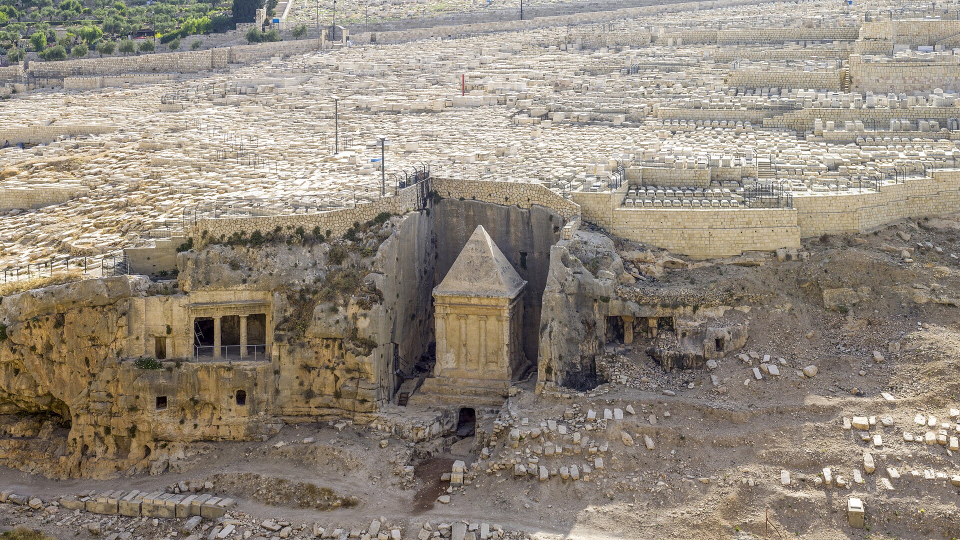 The Tomb of Benei Hezir in the Kidron Valley — a two-columned Doric facade cut into the rock face — with the pyramid-topped monolithic Tomb of Zechariah beside it.
