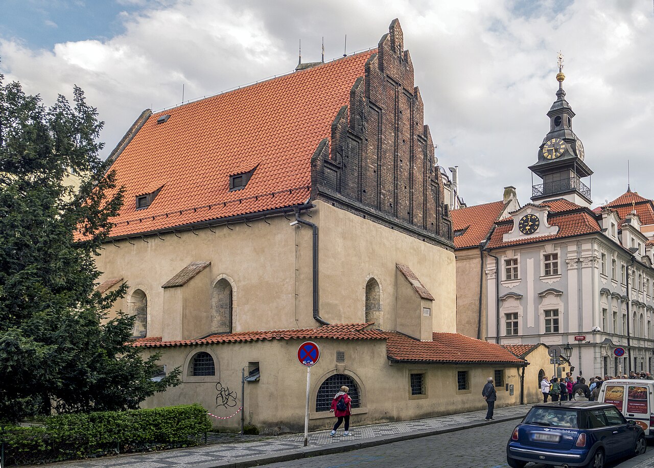 The Altneuschul (Old-New Synagogue) in Prague's Josefov quarter — the 13th-century Gothic hall with its steep saddle roof and late-Gothic brick gables, Europe's oldest active synagogue, with the clock tower of the Jewish Town Hall behind.
